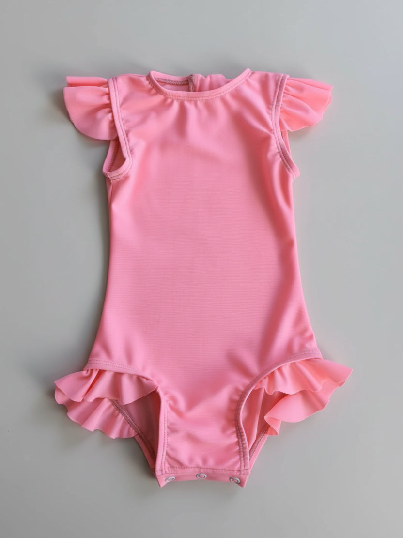 Pink baby romper with ruffled sleeves and bottom on a wooden surface