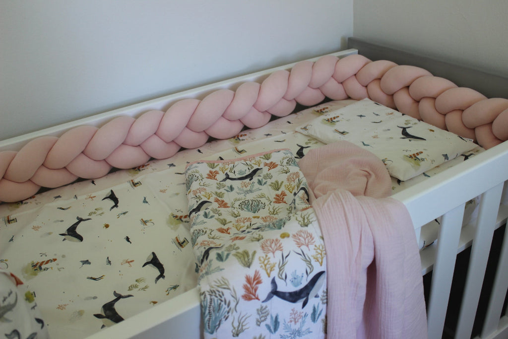 Crib with braided pink bumper and floral blanket