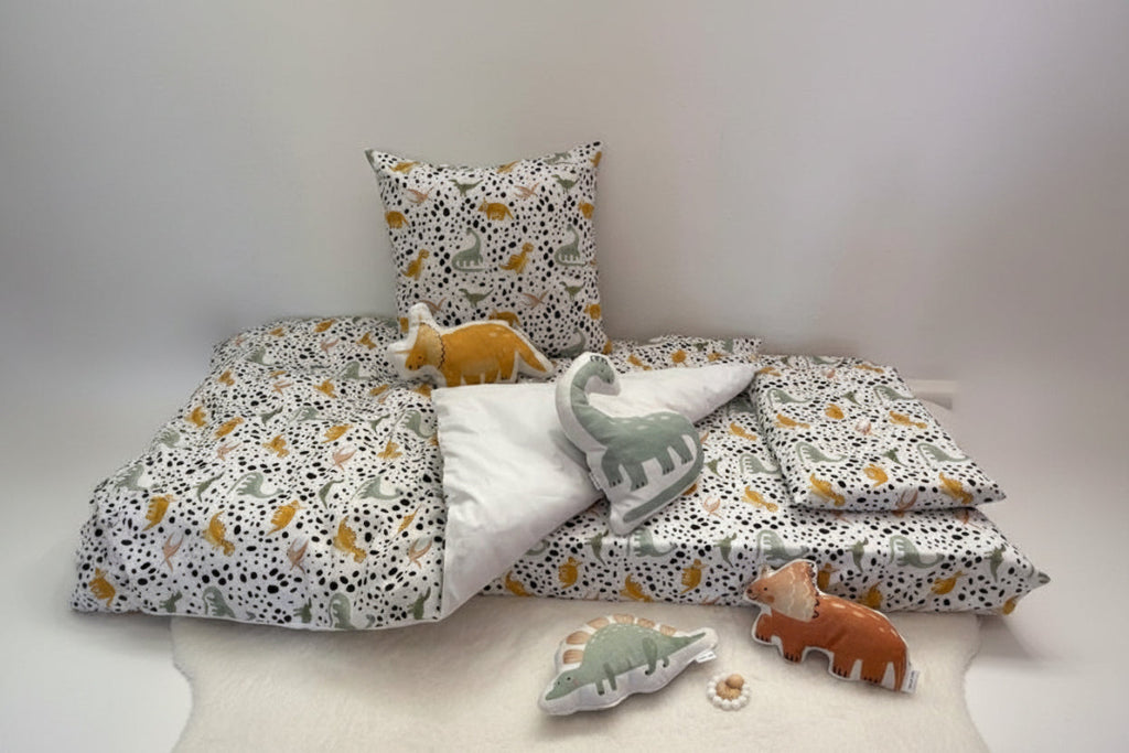 Children's bedding set with dinosaur pattern and plush toys on a bed.