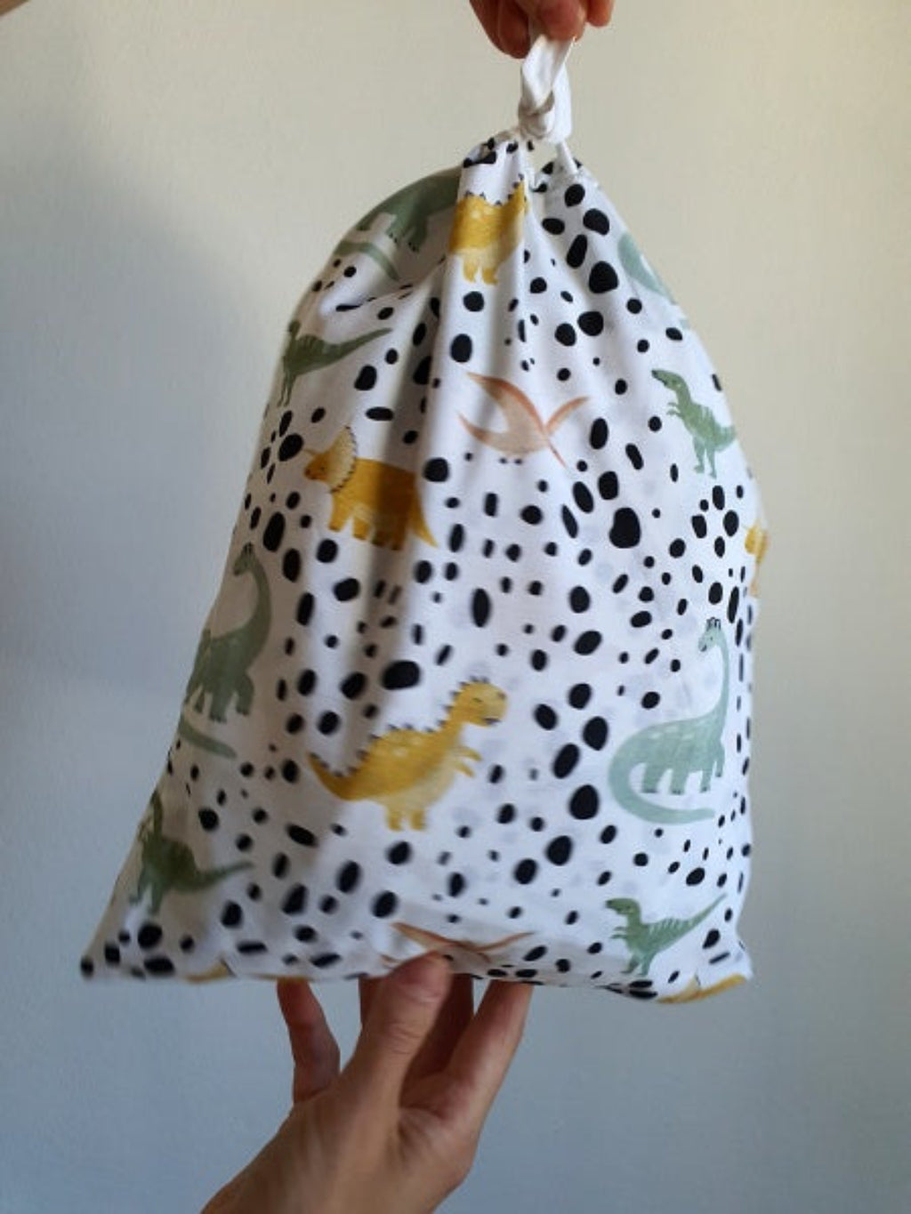 Drawstring bag with dinosaur pattern held by a hand against a plain background
