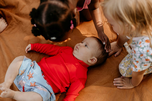 Children playing with a baby on a wooden floor wearing a swim shorts with built in nappy