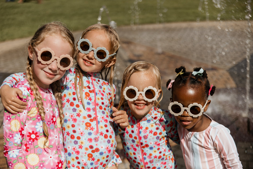 Four children wearing colorful sunglasses in front of a fountain.