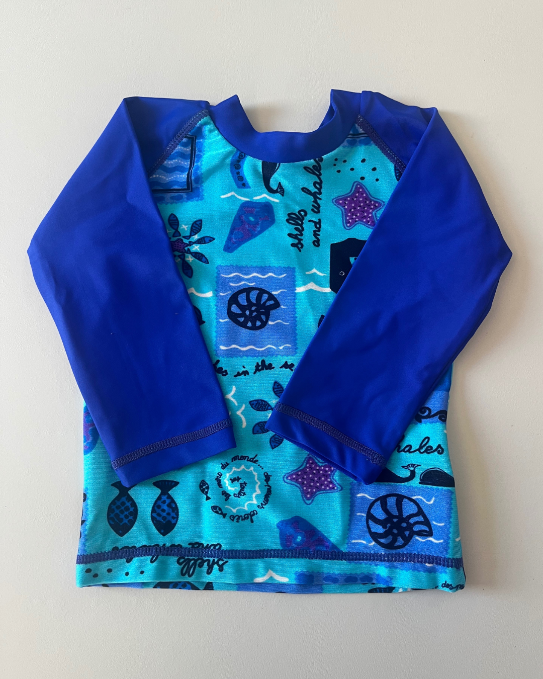Blue and turquoise children's swimsuit with sea-themed pattern on a white background