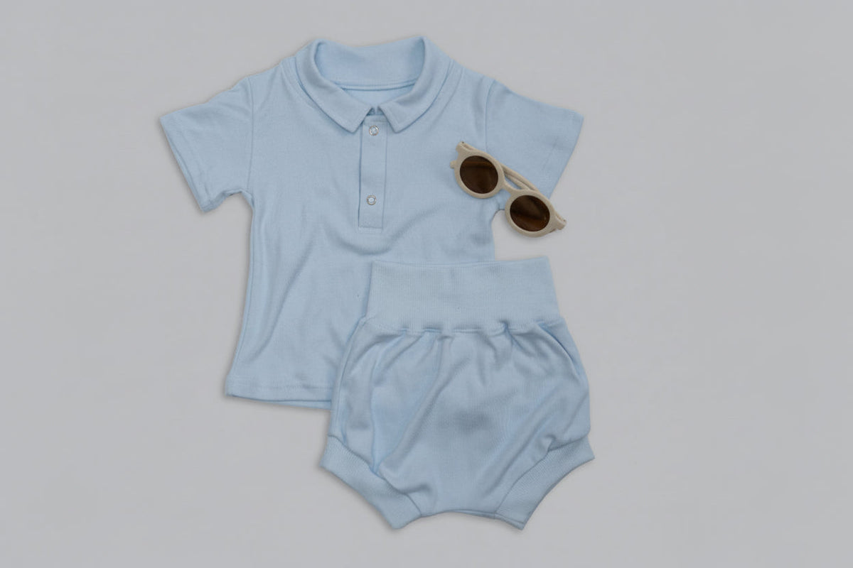 Light blue baby outfit with shorts, sippy cup, and sunglasses on a gray background