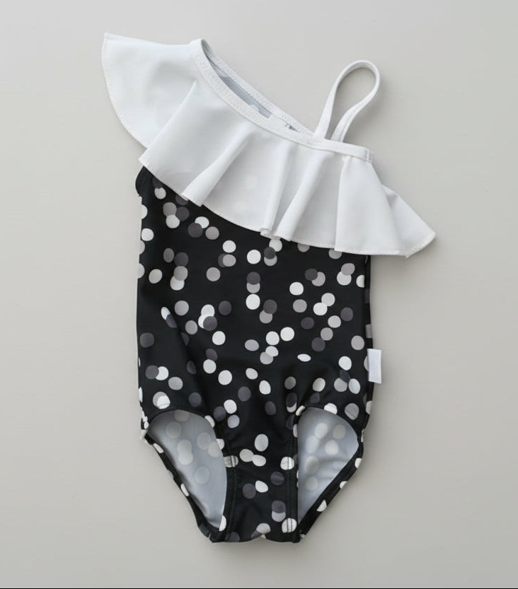 Black and white polka dot swimsuit with ruffled top on a wooden surface
