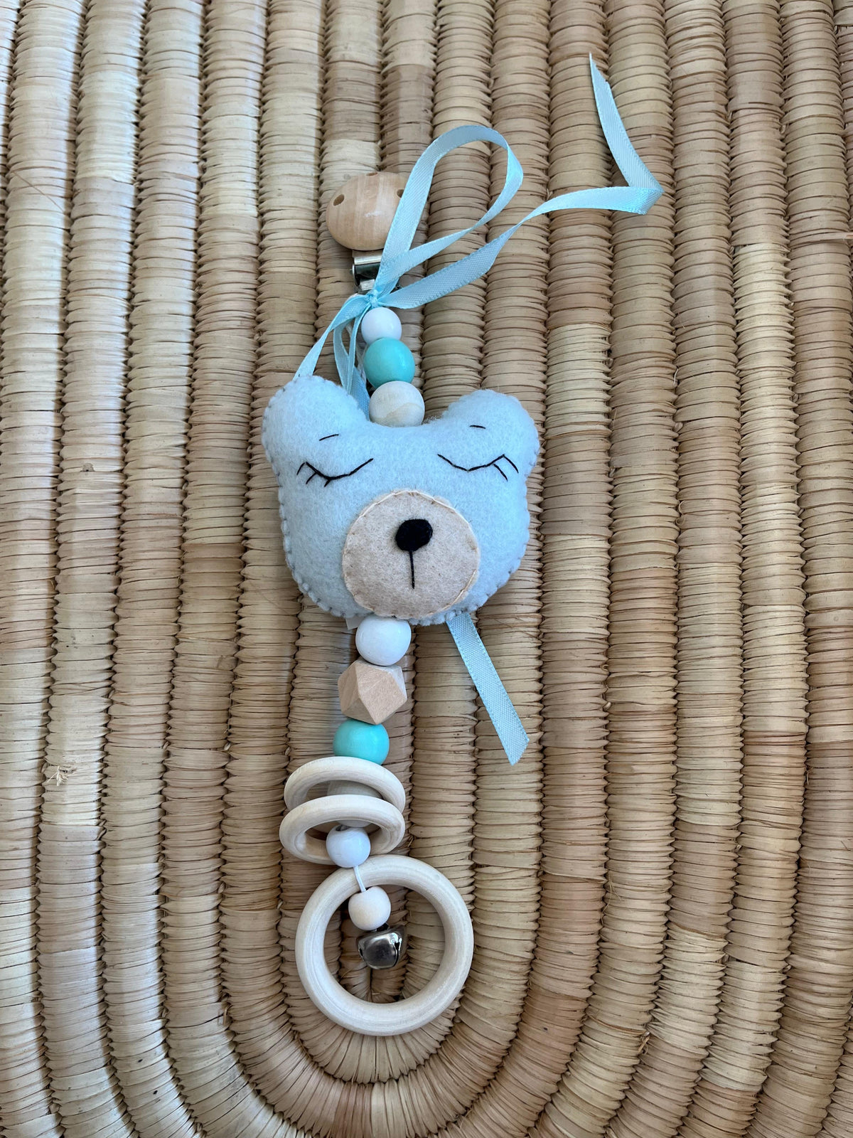 Felt teddy bear pram dangle with beads on a woven surface
