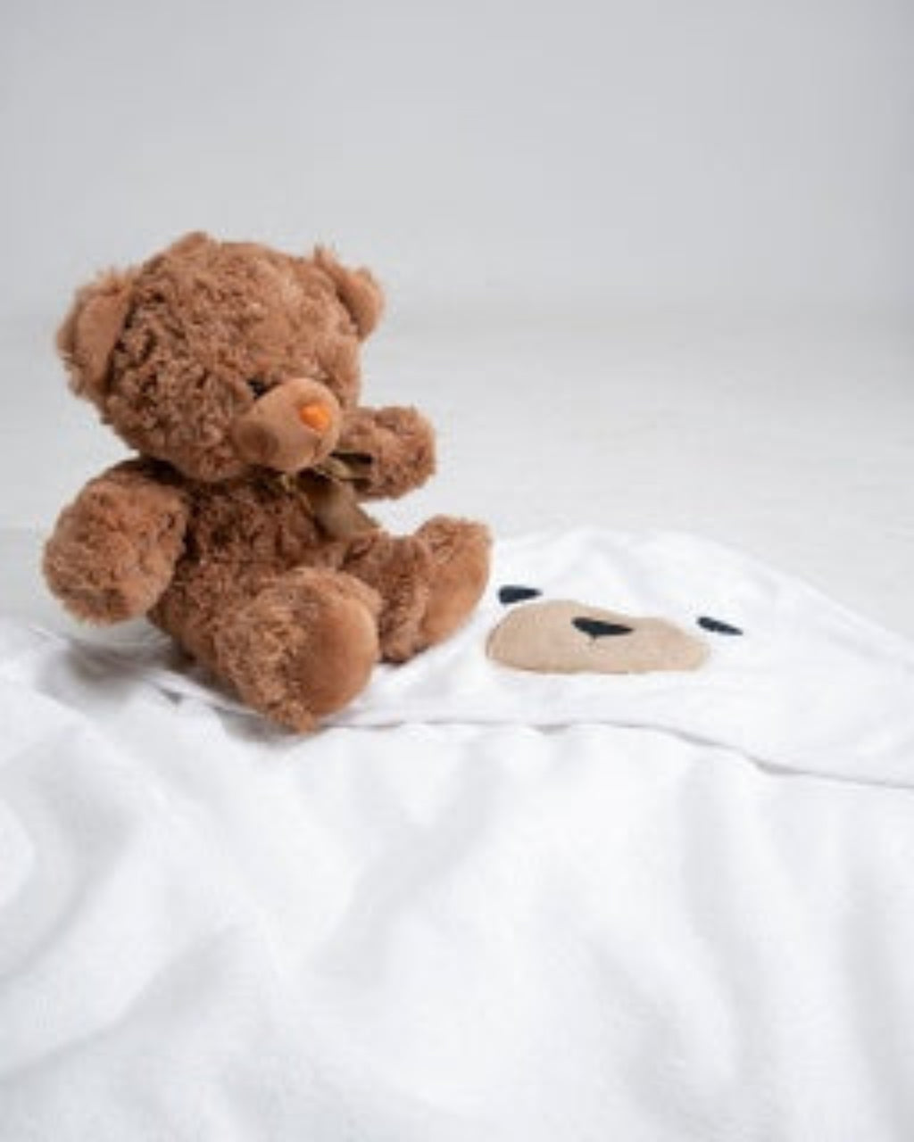 Brown teddy bear sitting on a white blanket with a cartoon face design.