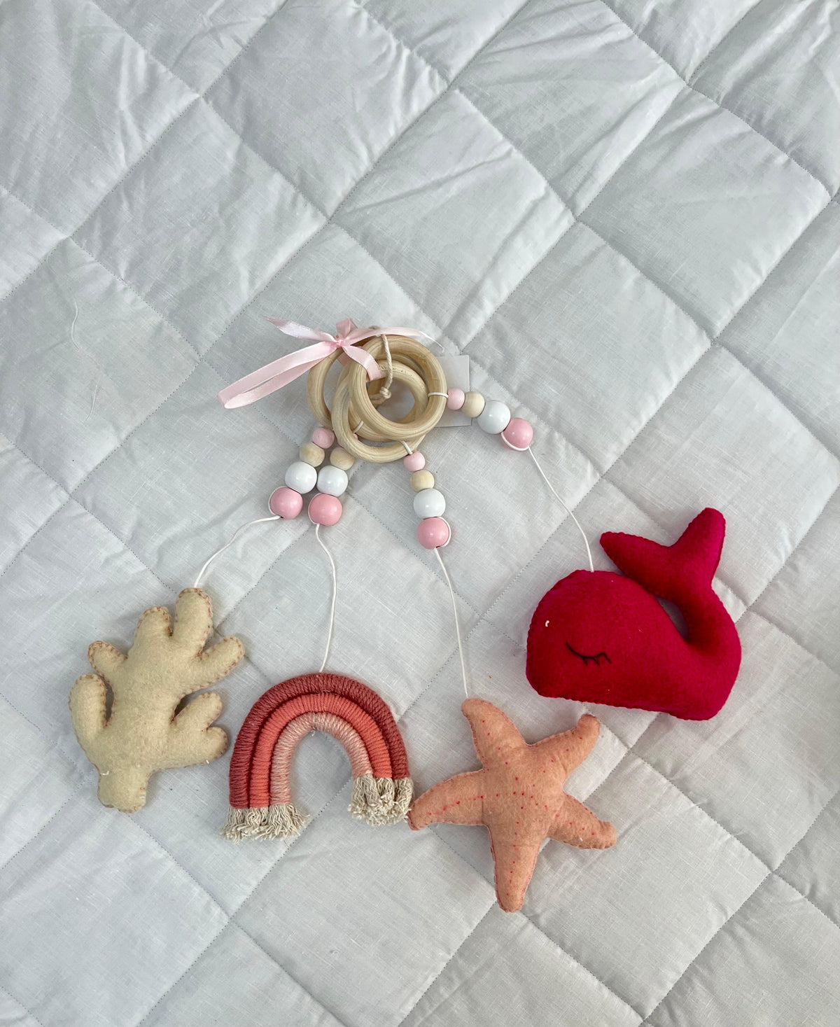 Set of soft toys including a whale, rainbow, starfish, and hand-shaped object on a textured fabric background.