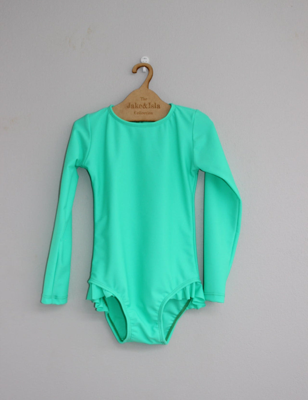 Green baby swimwear on a hanger against a gray background