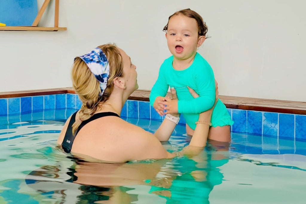 Woman and child in a pool, with the child wearing a green swimsuit.