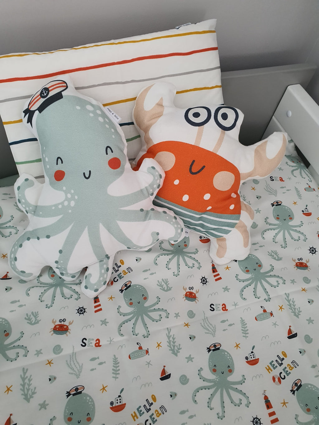 Children's room with decorative pillows featuring an octopus and a crab design on a bed with a sea-themed bedding set.