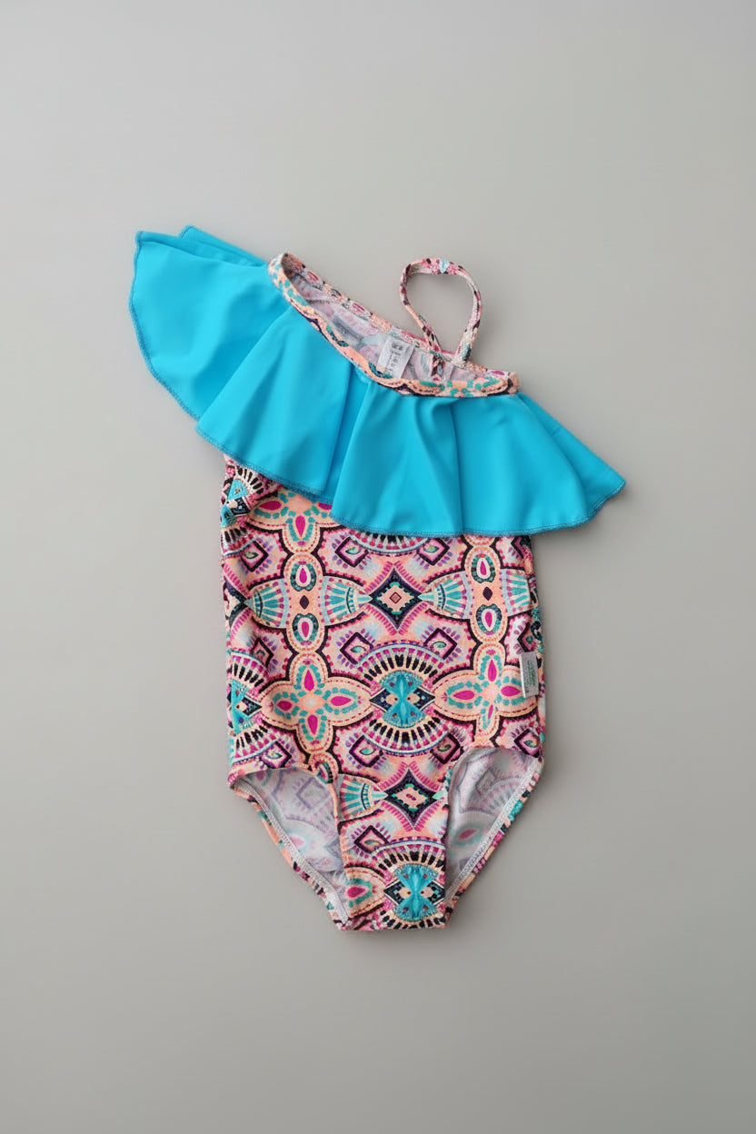 Multicolored patterned swimsuit with blue ruffled top on a wooden surface