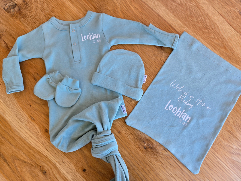 Baby outfit set with onesie, hat, and blanket on a wooden surface