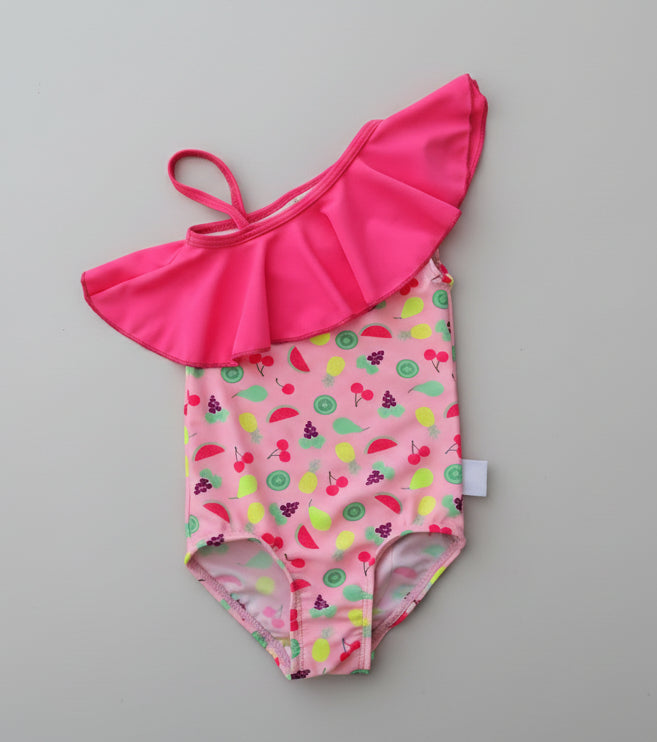 Pink children's swimsuit with fruit pattern and matching headband on a wooden surface