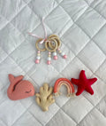 Set of baby toys including a pink whale, beige hand, rainbow, and red star on a textured white background.