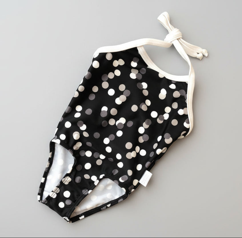 Black swimsuit with white polka dots on a green grass background