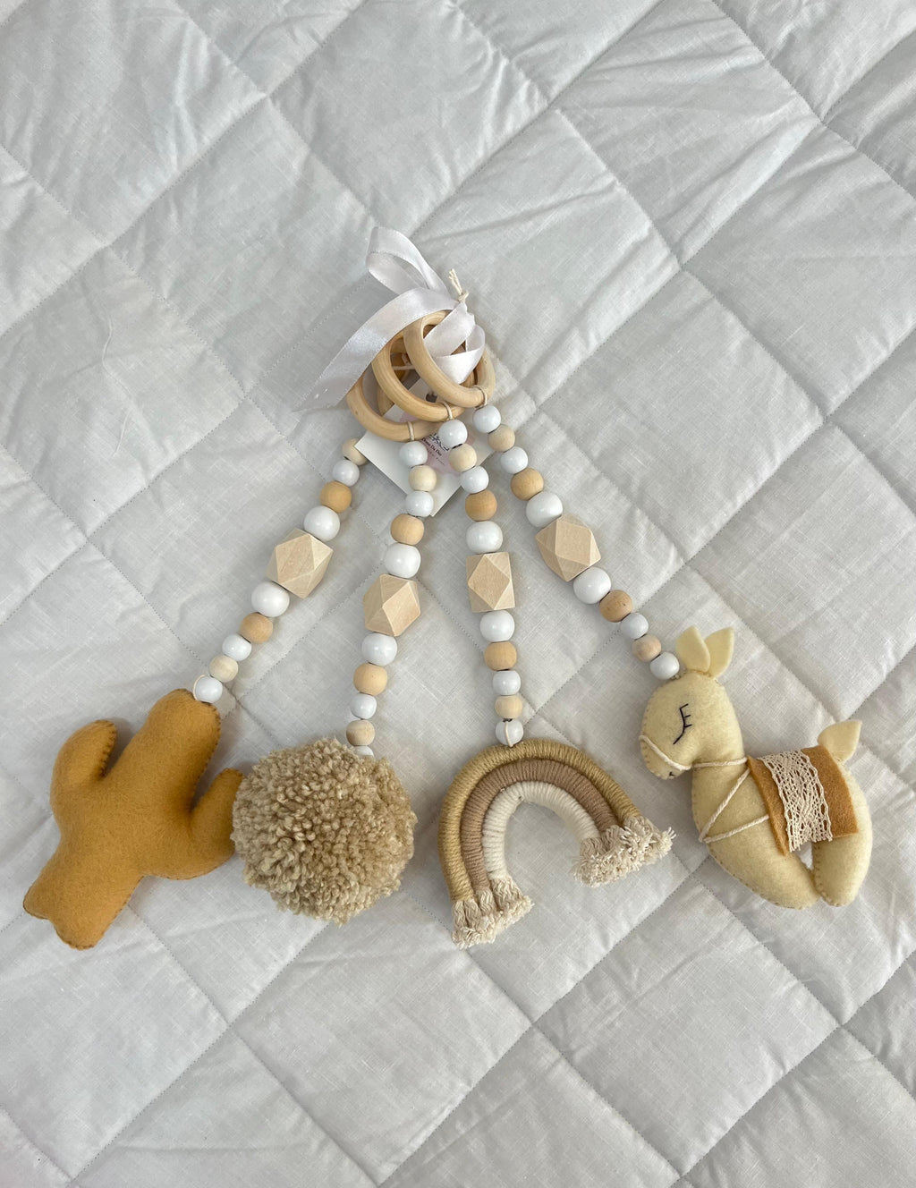 Baby mobile dangle toy with wooden elements and soft textures on a light gray quilted background
