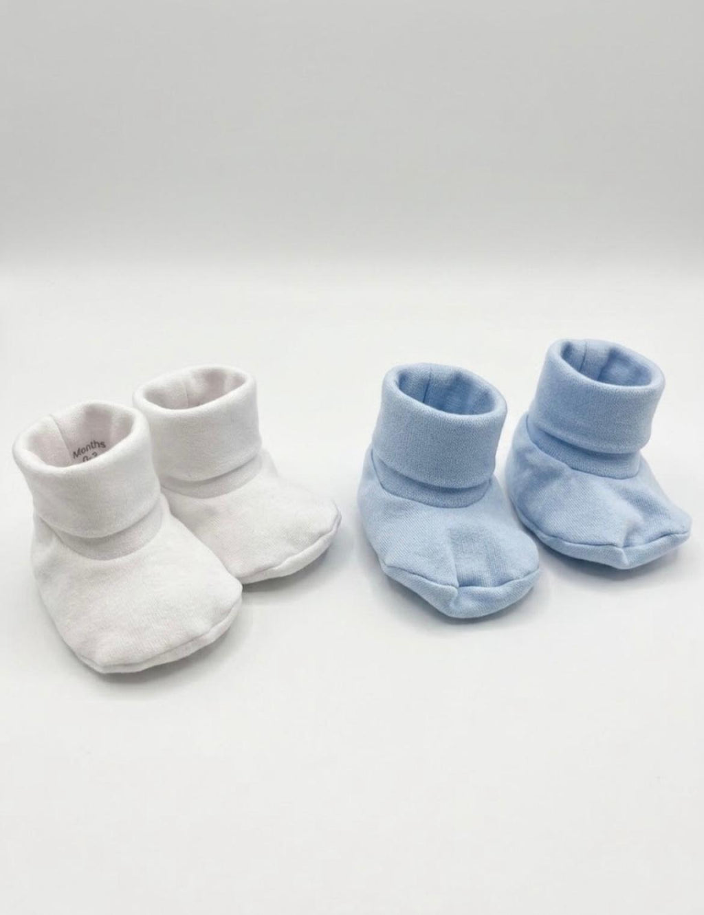 Two pairs of soft baby booties on a light gray background, one pair in white and the other pair in light blue.