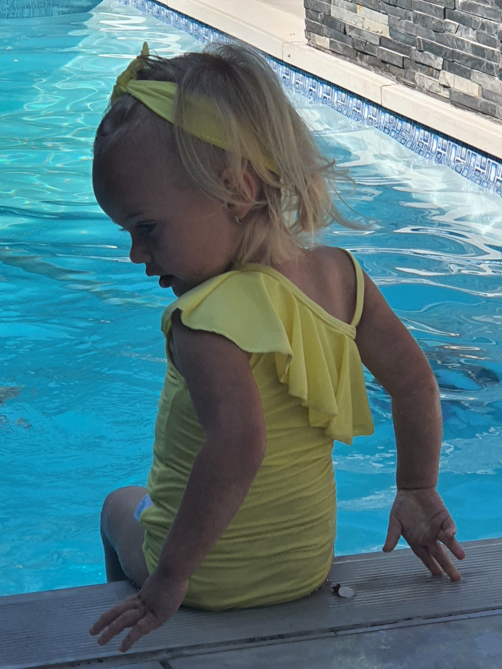 Child in a yellow swimsuit sitting by a pool